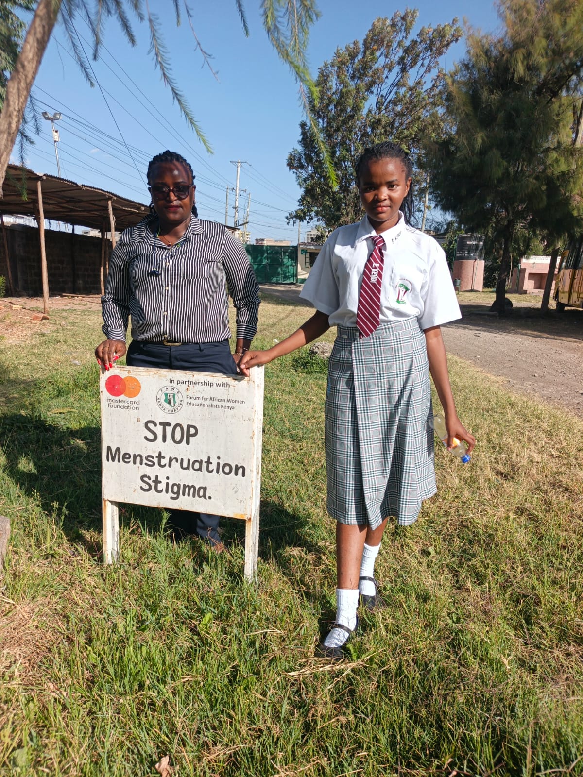 Ms. Jeruto Mukiri and a student standing beside a Stop Menstruation Stigma sign at Embakasi Girls High School